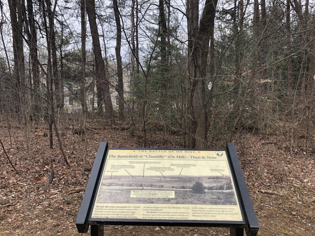 A wayside describes the historic landscape as modern housing is visible through the thin veil of trees at Ox Hill. - <i>Photo by the Author</i>